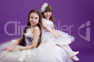 Two smiling little girls posing in elegant dresses
