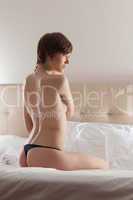 Profile of young naked woman sitting on bed