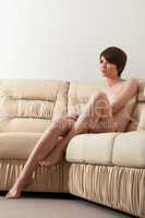 Naked brunette posing on beige leather sofa