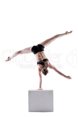 Slim acrobat balancing on cube in studio