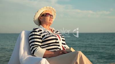 Senior woman resting on the seacoast at sunset