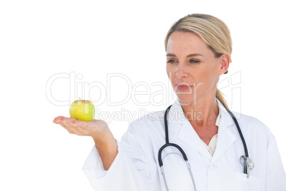 Smiling doctor holding apple and looking at it