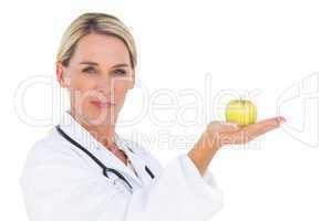 Happy doctor holding out green apple and looking at camera