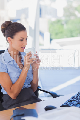 Businesswoman holding her mug and looking at her computer