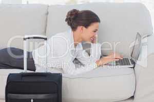 Business woman lying on couch with laptop and suitcase