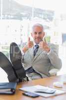 Happy businessman giving thumbs up with feet up