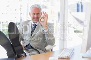 Happy businessman giving ok sign with feet up