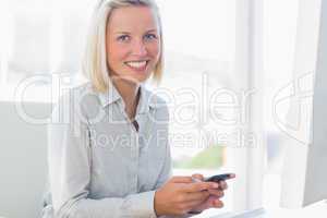 Blonde businesswoman texting and smiling at camera