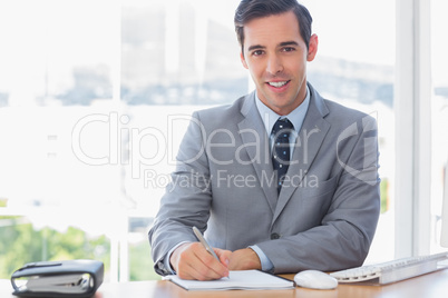 Smiling businessman writing at his desk