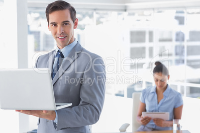 Businessman standing with laptop and smiling at camera