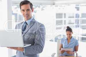 Businessman standing with laptop and smiling at camera