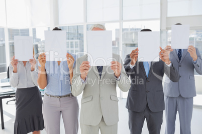 Buisness team holding up blank pages and covering their faces