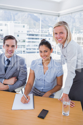 Business people at desk with notepad smiling at camera