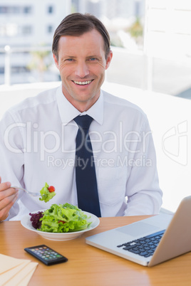 Cheerful businessman eating a salad on his desk