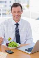 Cheerful businessman eating a salad on his desk