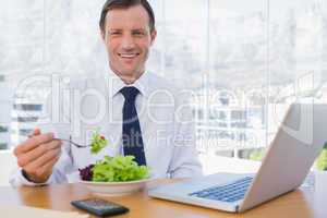 Happy businessman eating a salad on his desk
