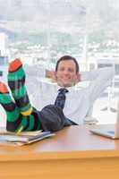 Cheerful businessman relaxing with feet on his desk