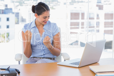 Brunette businesswoman cheering in front of her laptop