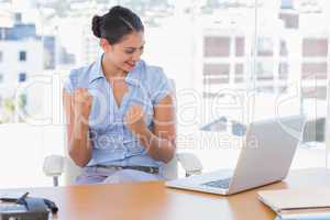 Brunette businesswoman cheering in front of her laptop