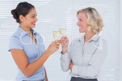 Two cheerful colleagues clinking their flutes of champagne