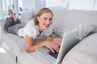 Businesswoman lying on couch using her laptop