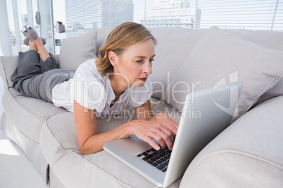 Businesswoman lying on couch and using laptop