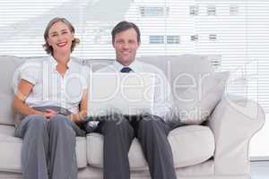 Two colleagues sitting on couch using laptop in bright office