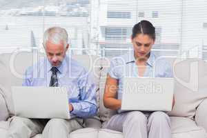 Business people sitting on sofa using their laptops