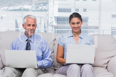 Business people sitting on sofa using their laptops and smiling