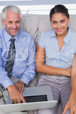 Business people using laptop on the couch and smiling up at came