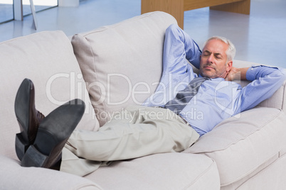 Businessman lying on sofa with his feet up