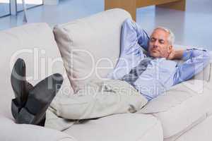 Businessman lying on sofa with his feet up