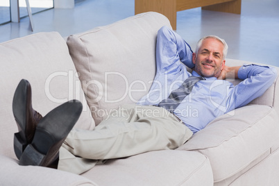 Businessman lying on sofa with his feet up smiling at camera