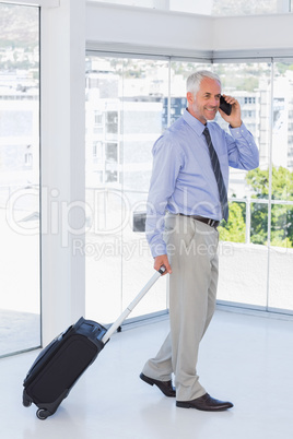 Businessman pulling suitcase and talking on phone