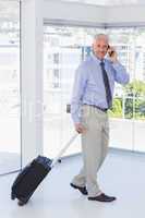 Businessman pulling suitcase and talking on phone smiling at cam