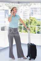 Smiling businesswoman on the phone leaning on suitcase