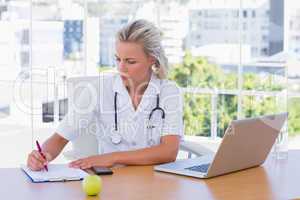 Blonde nurse writing on a notepad on her desk