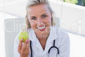 Smiling blonde nurse holding a green apple