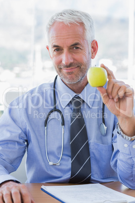 Doctor sitting behind his desk holding an apple