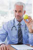 Doctor sitting behind his desk holding a green apple