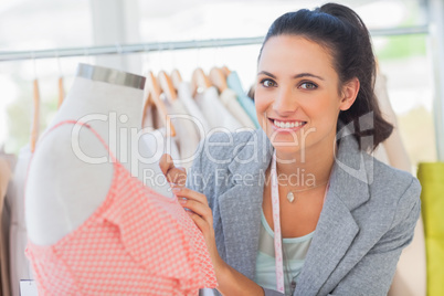 Smiling fashion designer measuring dress on a mannequin