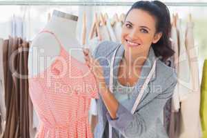 Smiling fashion designer fixing dress on a mannequin