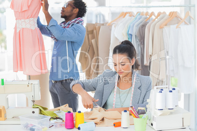 Fashion designer cutting textile at desk