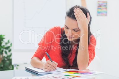 Tired designer holding her head while she is drawing