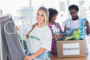 Cheerful volunteers putting clothes in clothes rail