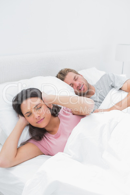 Woman covering her ears while her husband is snoring