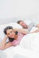 Woman covering her ears while her husband is snoring