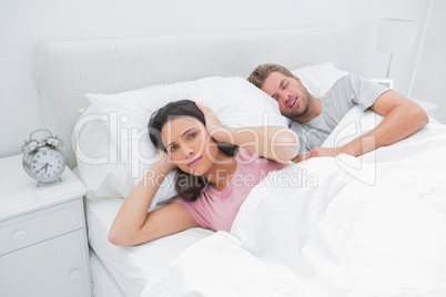 Snoring man is annoying his wife who tries to sleep