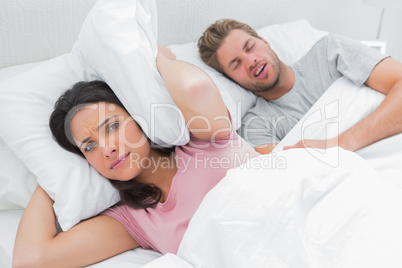 Woman covering ears with pillow while her husband is snoring