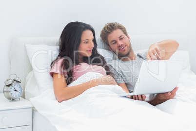 Couple lying in bed looking at a laptop